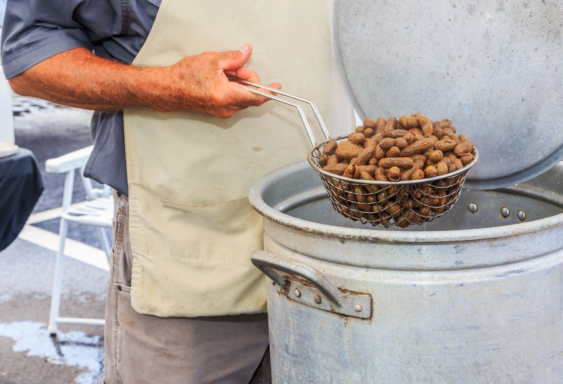 Person holding a strainer of boiled peanuts over a large pot.