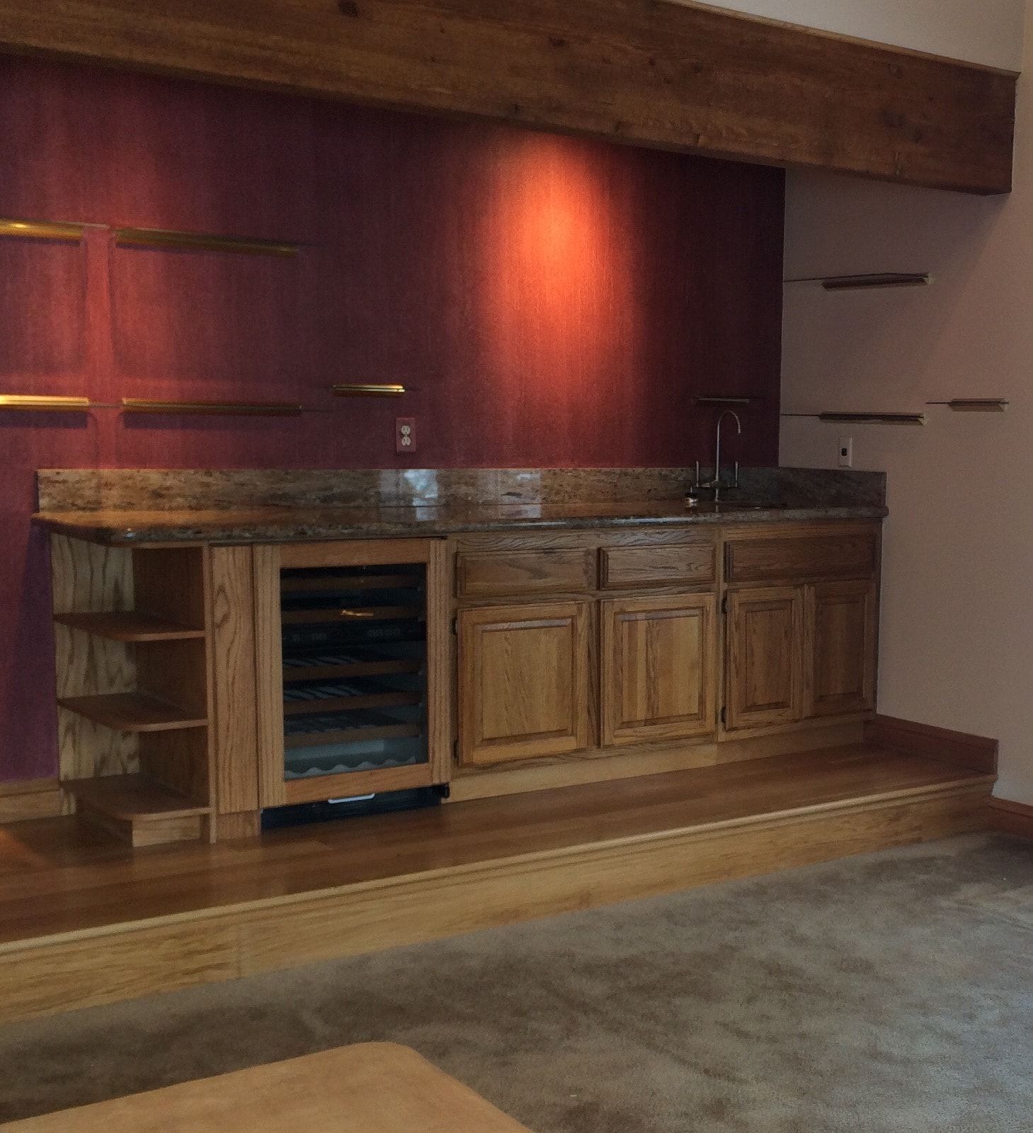 Built-in home bar with wood cabinets, wine cooler, granite countertop, and red textured wall.