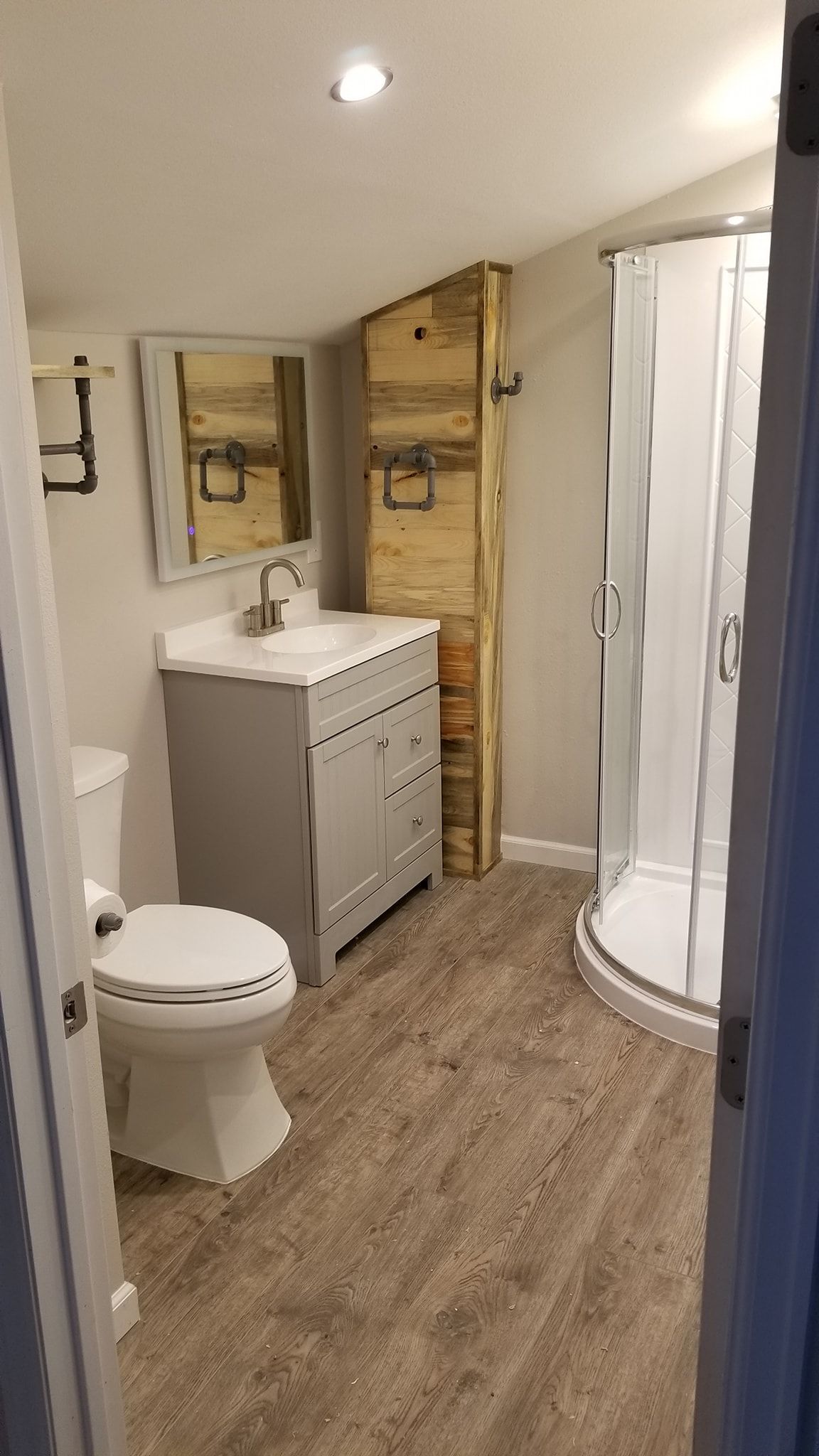 Bathroom with gray vanity, toilet, shower, and rustic wooden cabinet.