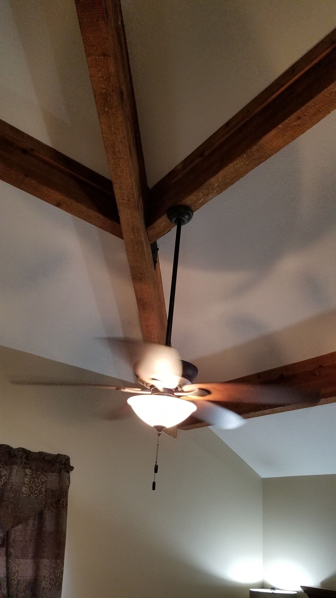 Ceiling fan with light fixture suspended from wooden beams in a room.