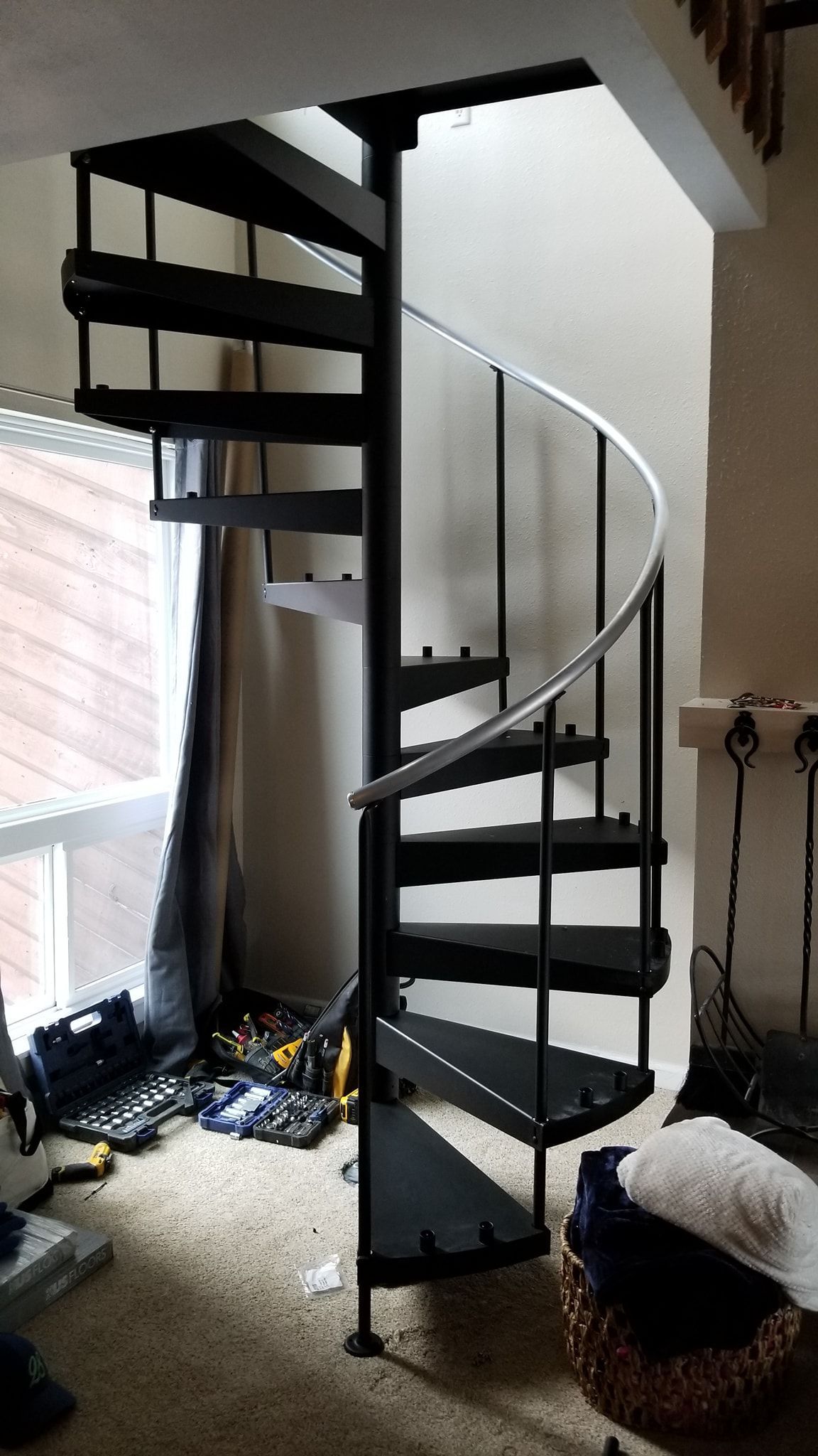 Black spiral staircase in a room with tools on the floor.