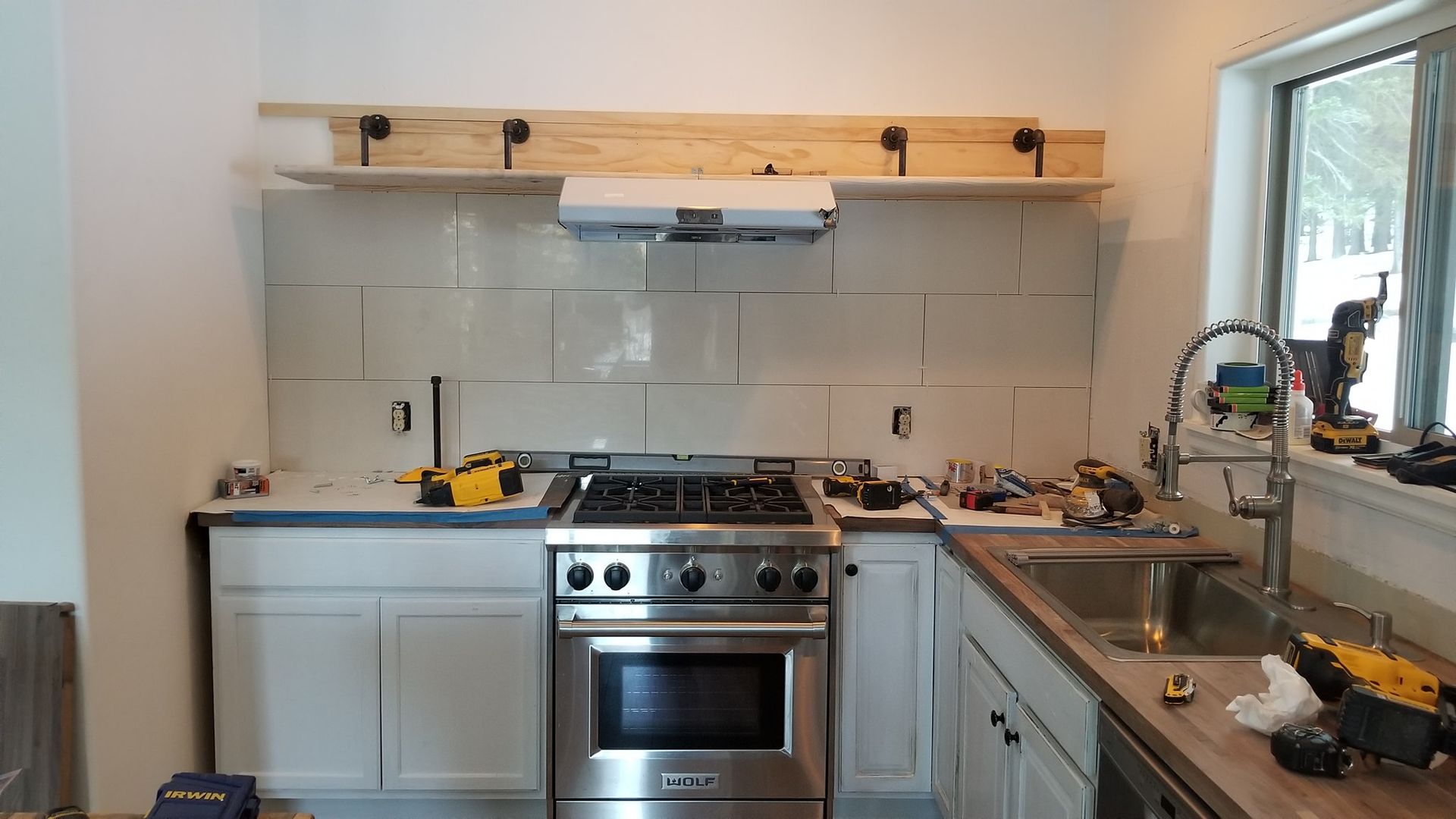 Kitchen under construction, with a stove, sink, cabinets, and partially installed backsplash.