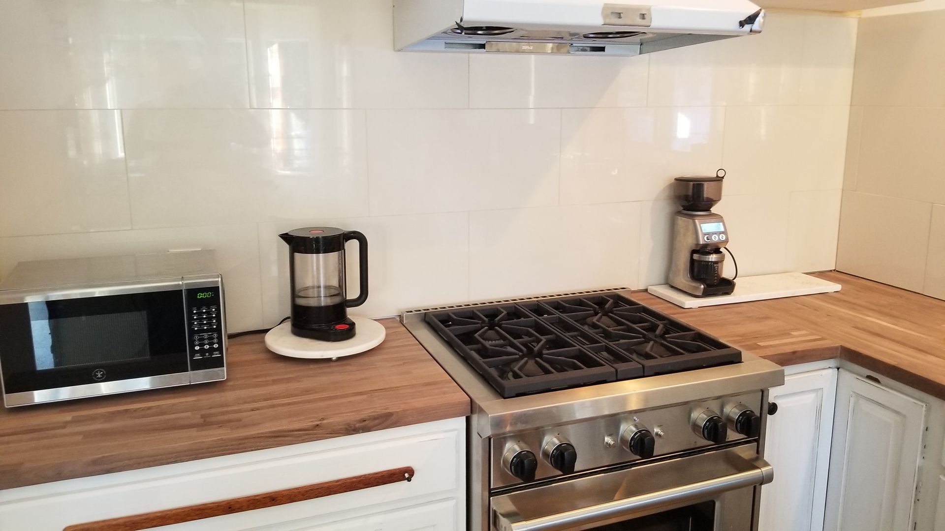 Kitchen corner with appliances: microwave, blender, gas stove, and coffee maker on wooden countertops.