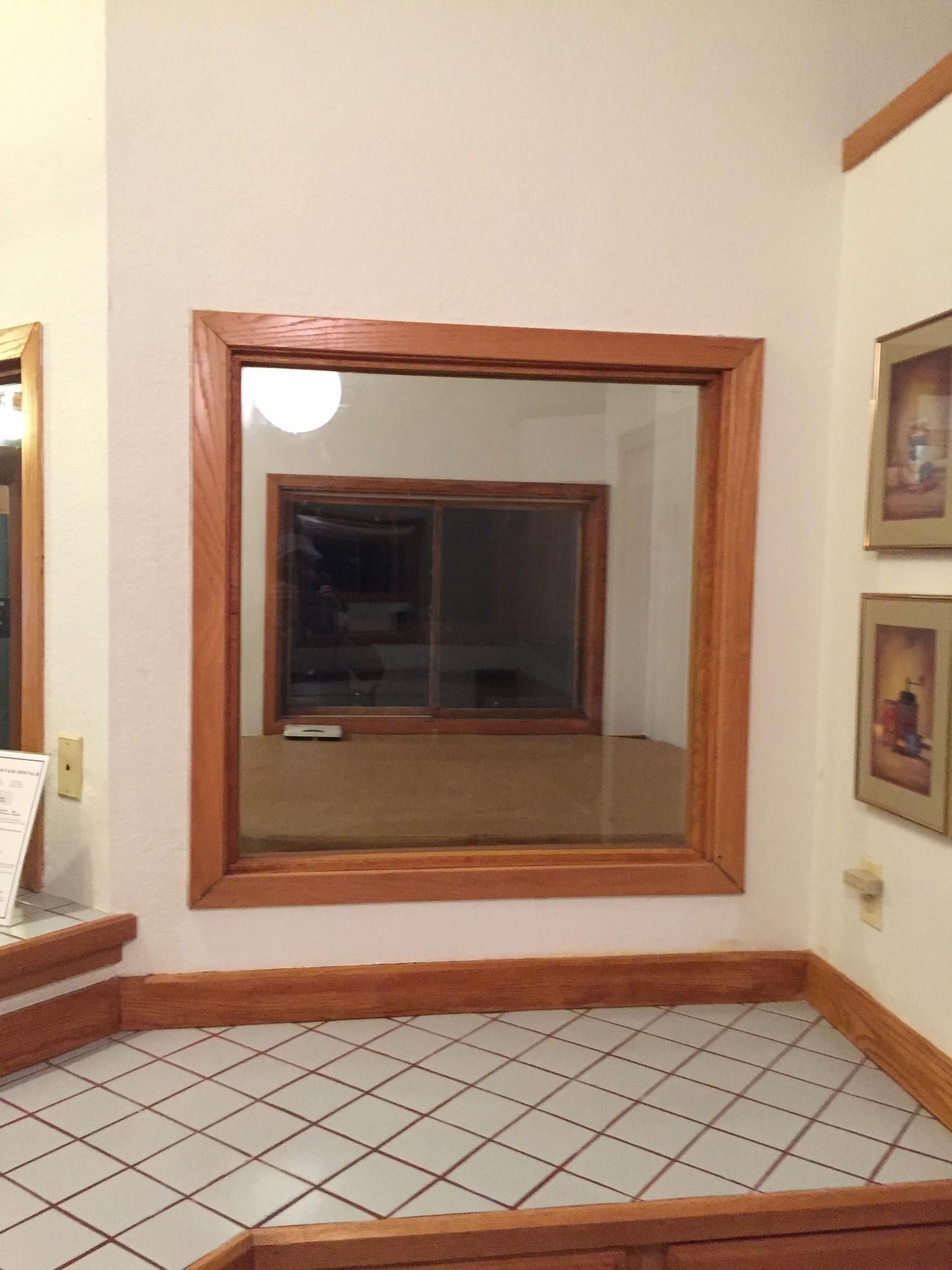 Mirror reflecting a room with a sliding glass door and wooden trim. Tile floor in foreground.
