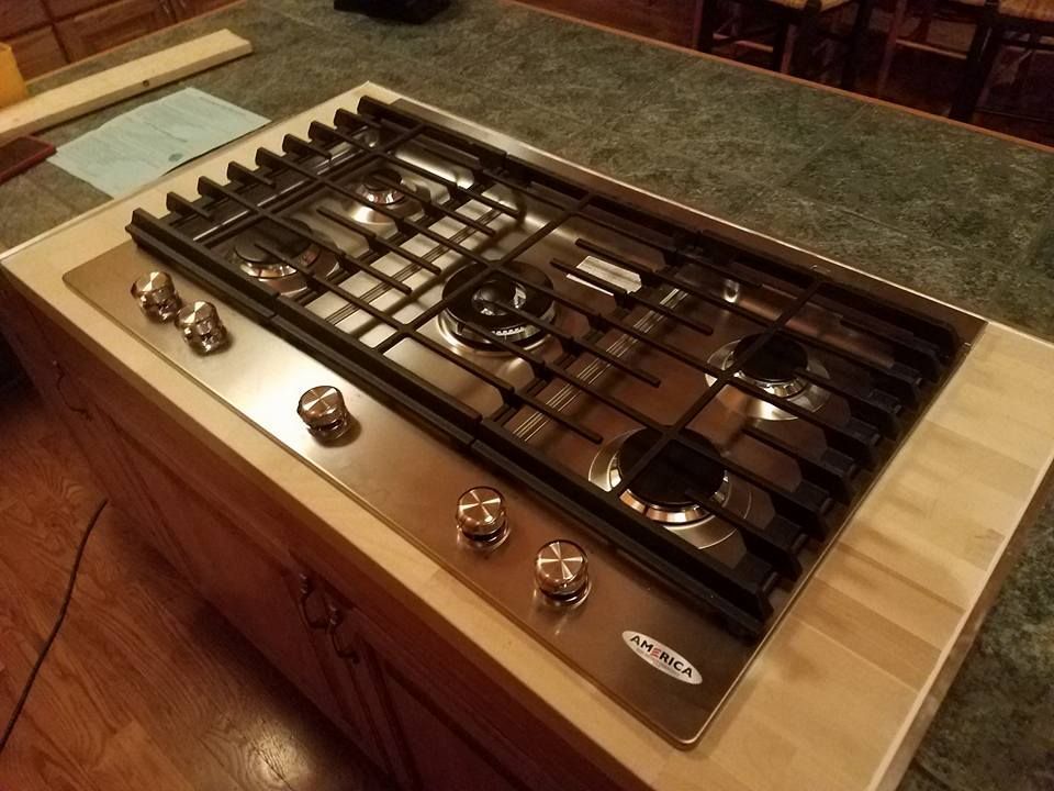 Stainless steel gas cooktop set into a countertop with four burners and control knobs.