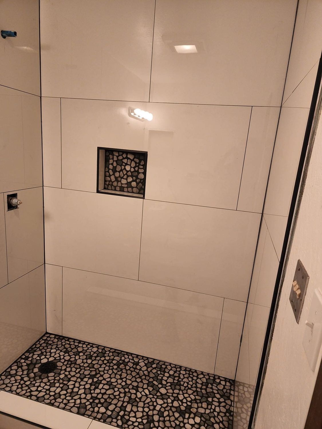 Shower with pebble floor, white tile walls, built-in shelf, glass door.