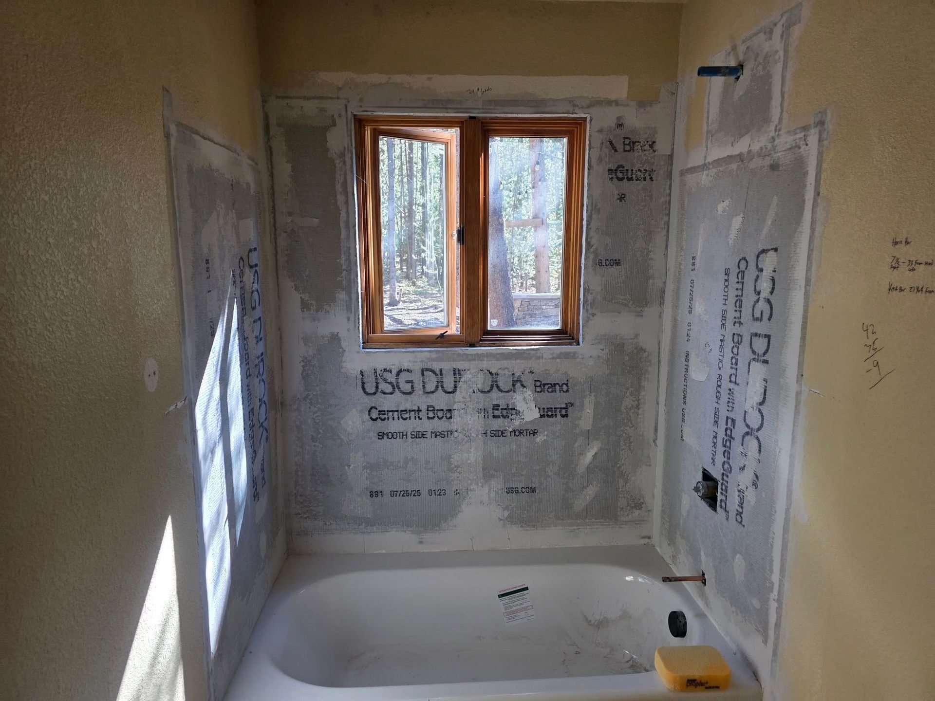 Bathroom remodel in progress with a tub, window, and wall panels.