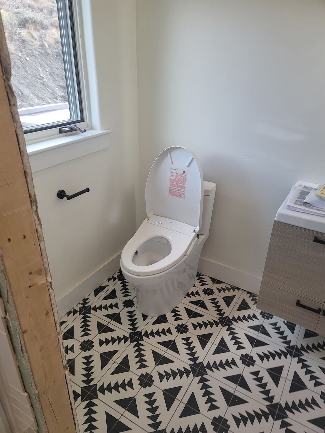 White toilet with an open seat, black patterned floor, and a small window.