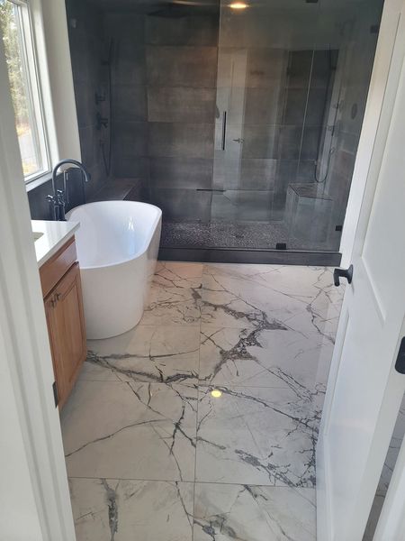 Modern bathroom with white soaking tub, marble floor, and gray tiled shower.
