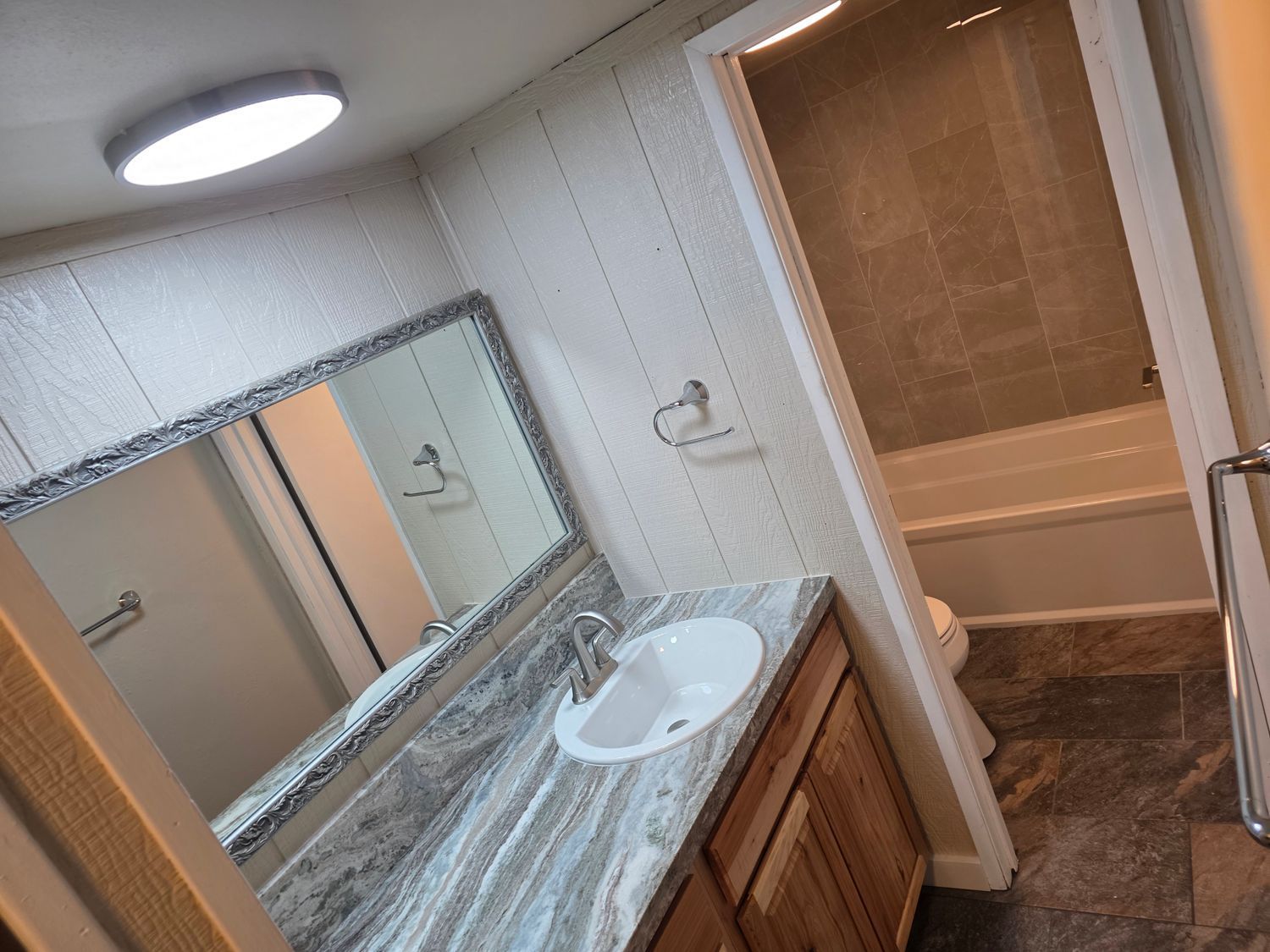Bathroom with sink, mirror, and a view into the shower/tub area. Brown and white tones.