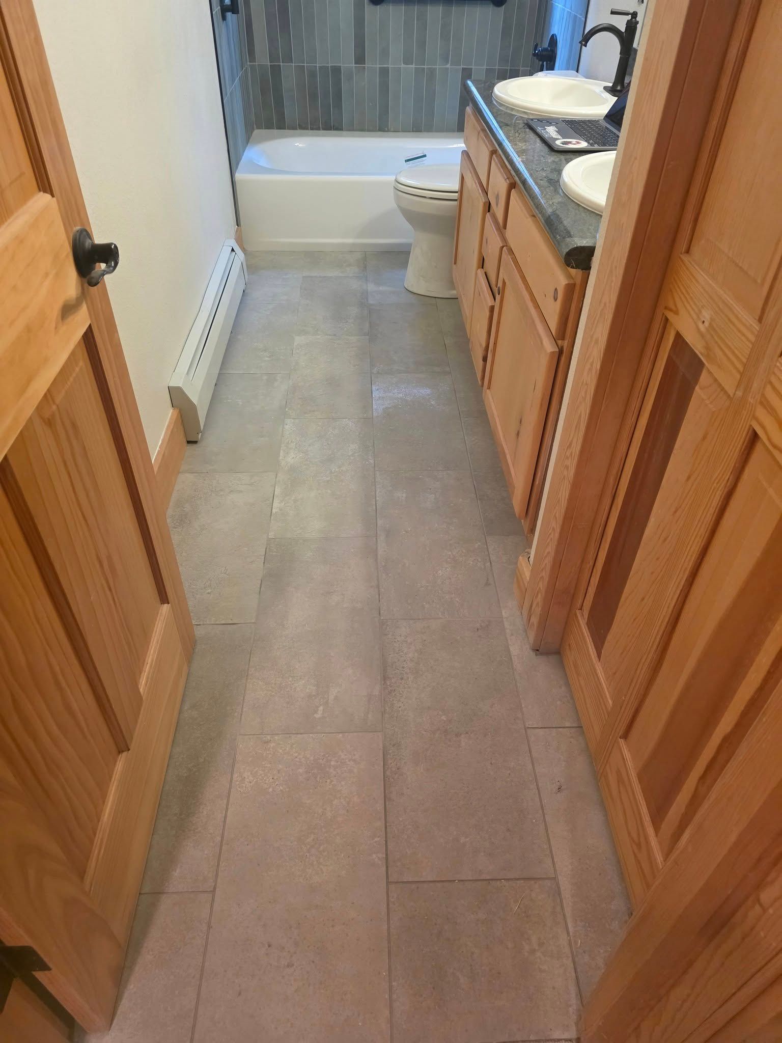 Bathroom interior with light-colored tile floor, wooden cabinets, and a bathtub with gray tile backsplash.