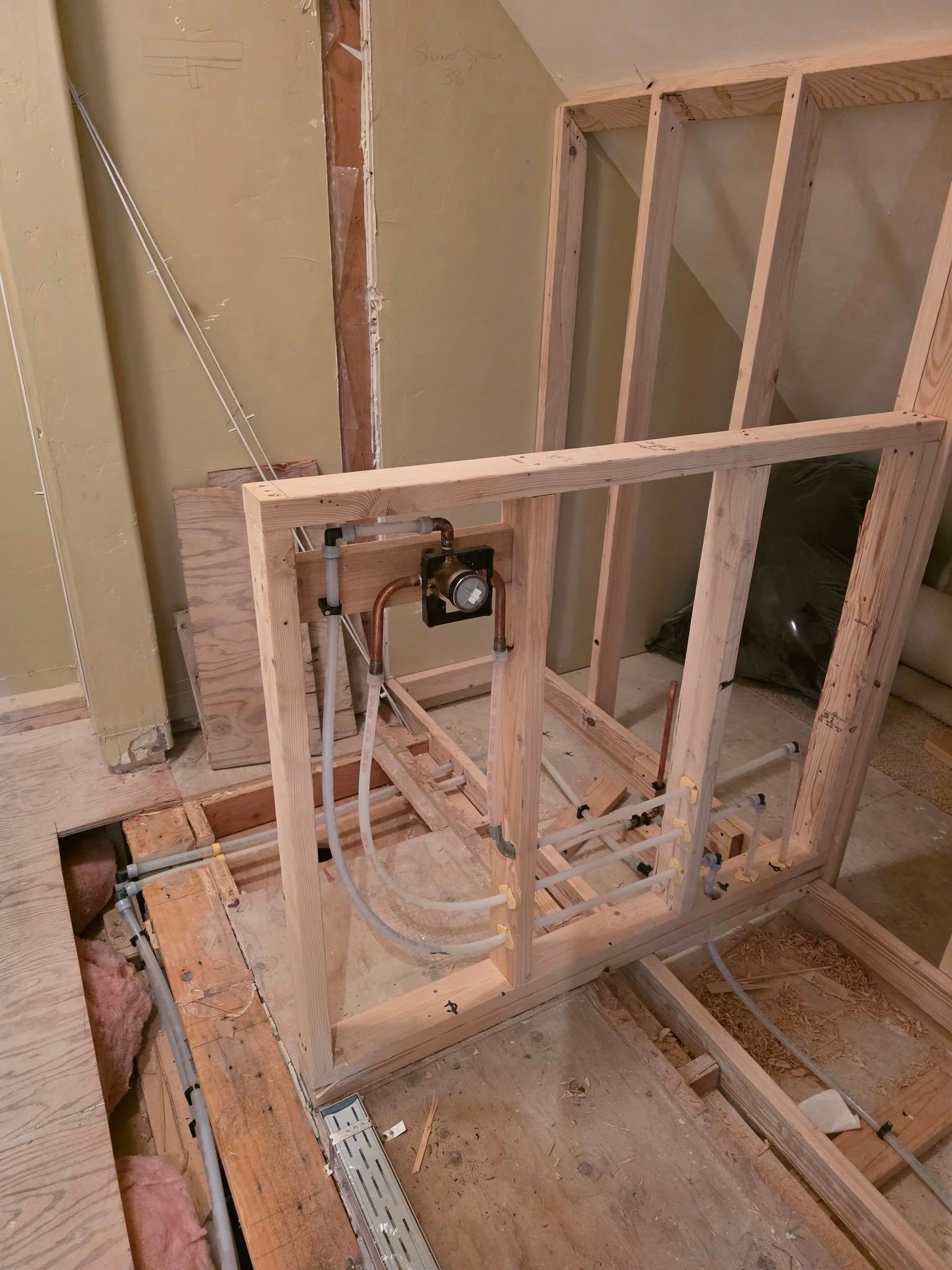 Bathroom under construction with exposed wood framing, electrical box, and plumbing.