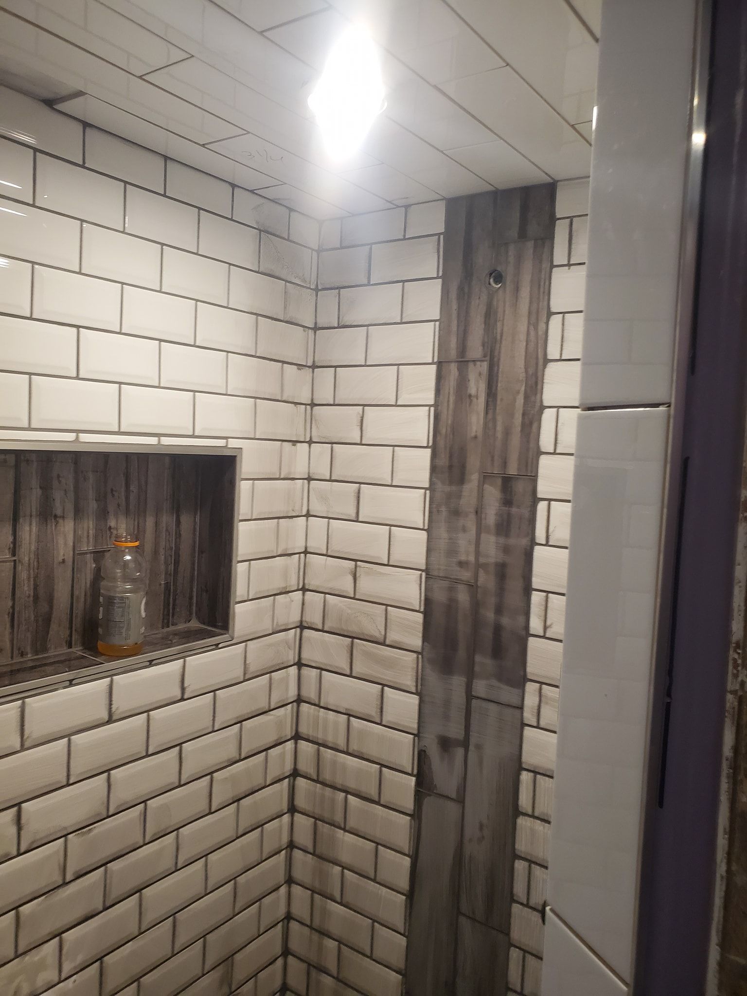 Tiled shower with a wooden accent, including a recessed shelf with a bottle.