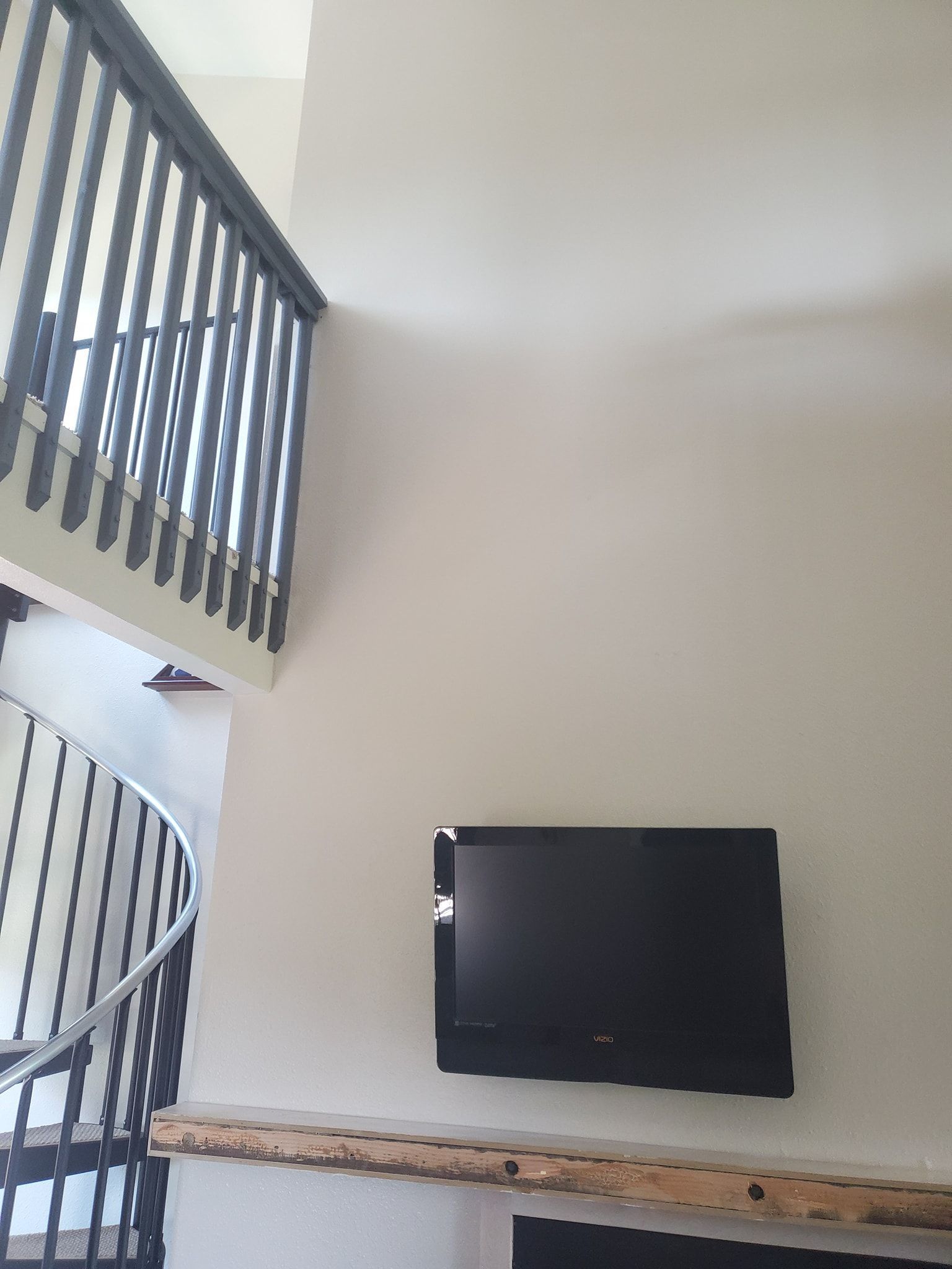 Interior with a spiral staircase, mounted TV, and light-colored walls.