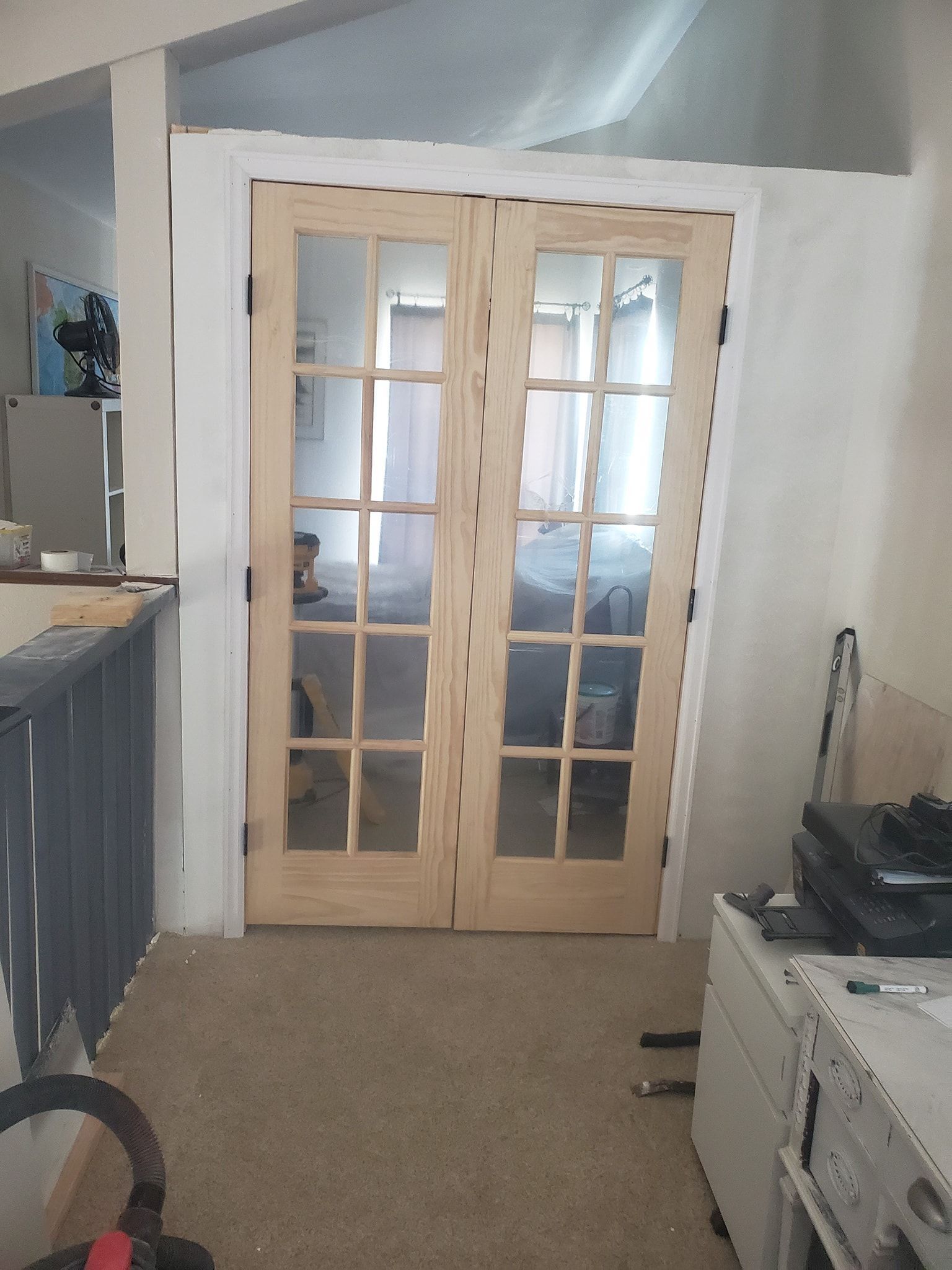 Double glass-paned doors with light wood frames leading to a room, flanked by white trim and walls.