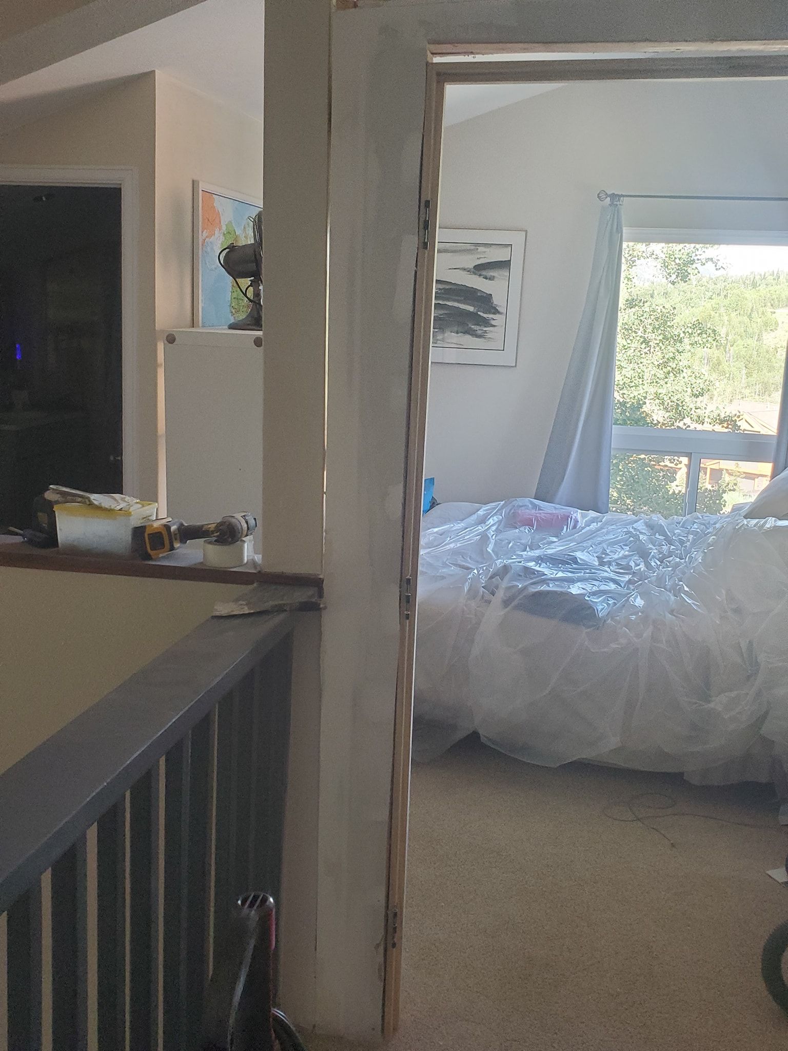 View through doorway to a bedroom with unmade bed, light streaming in from the window.