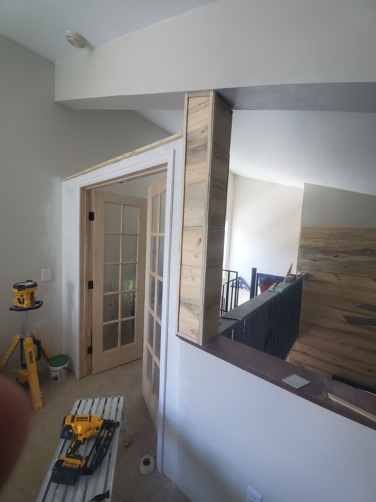 Renovation: Interior view of a partially constructed wall with wood siding, a doorway, and a railing.