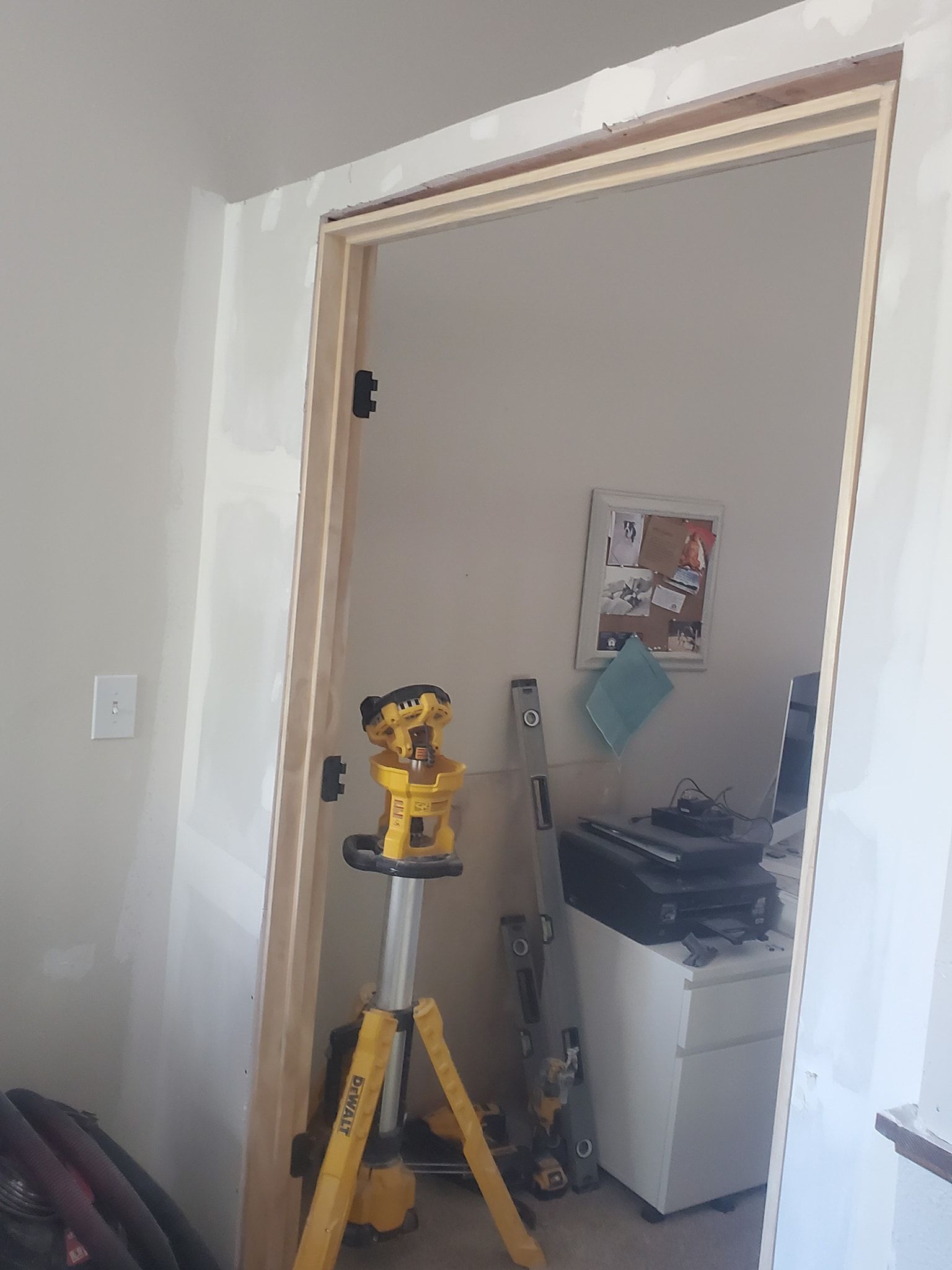 Door frame with a laser level on a tripod; interior office visible.
