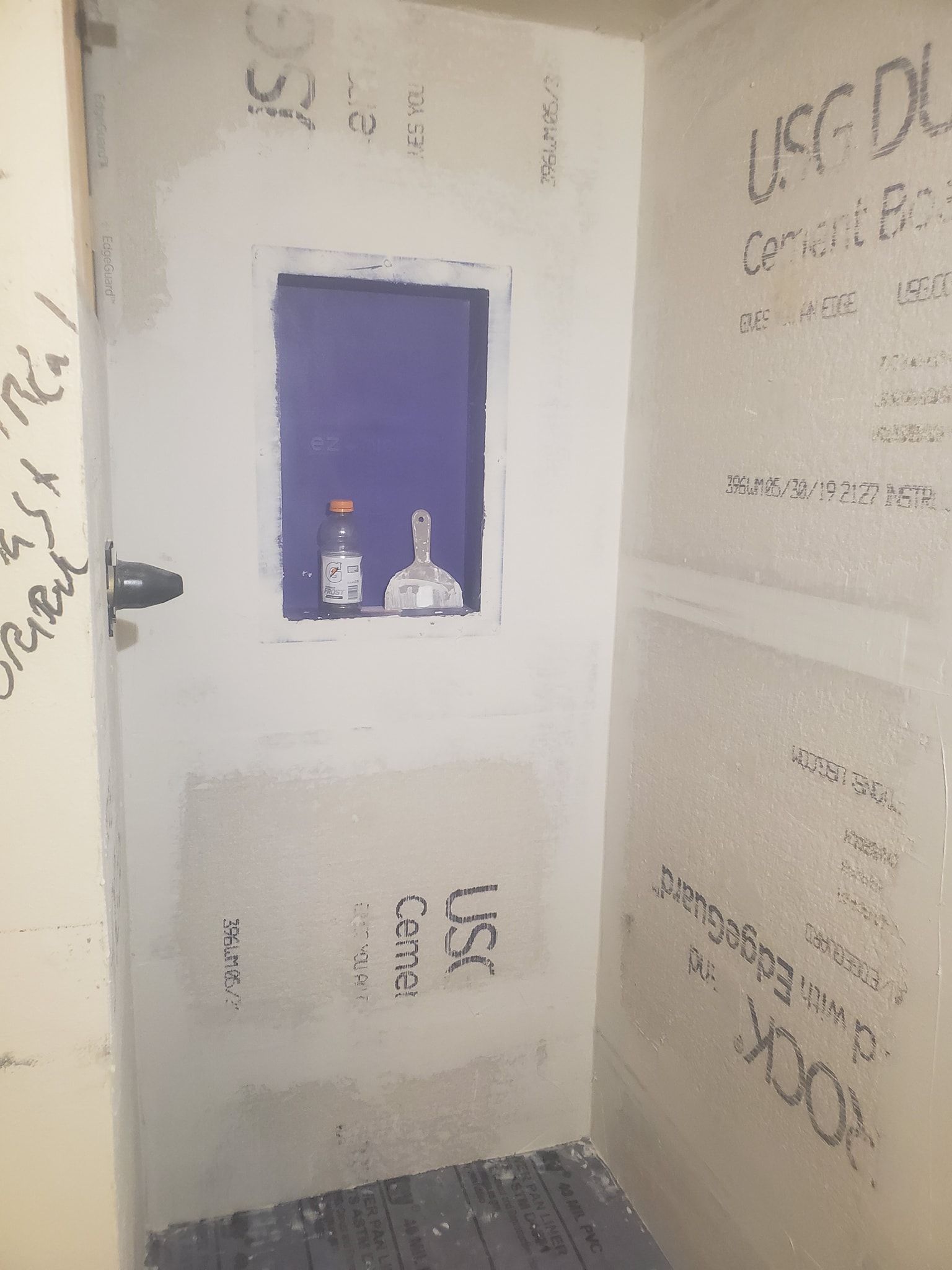 Shower stall under construction, with a recessed shelf containing two bottles; cement board walls.