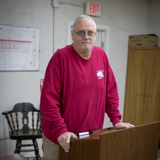 Man in red shirt standing in front of a podium in classroom
