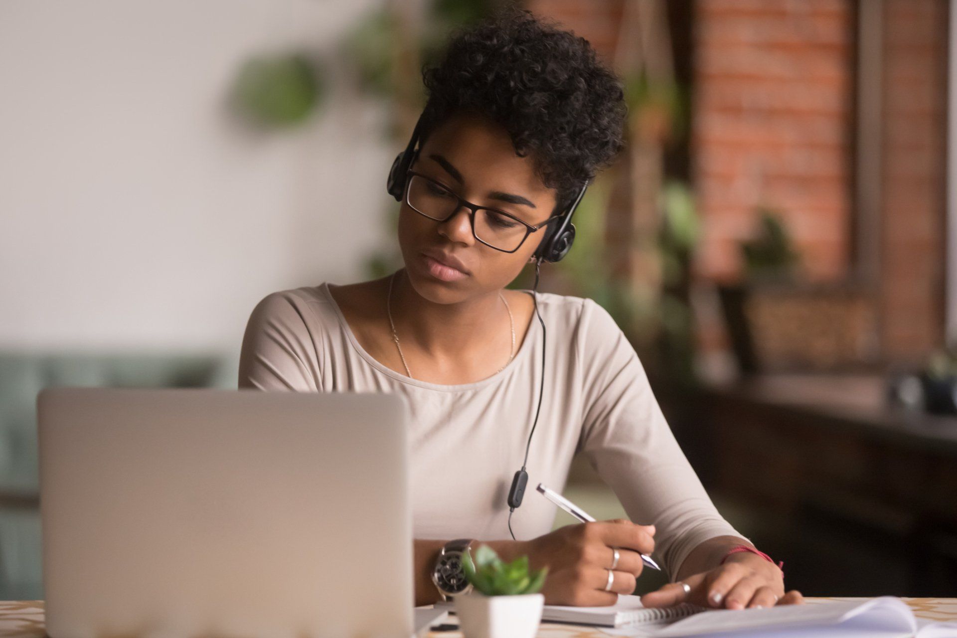 African American woman with headseat on staring at computer while taking notes for driving school