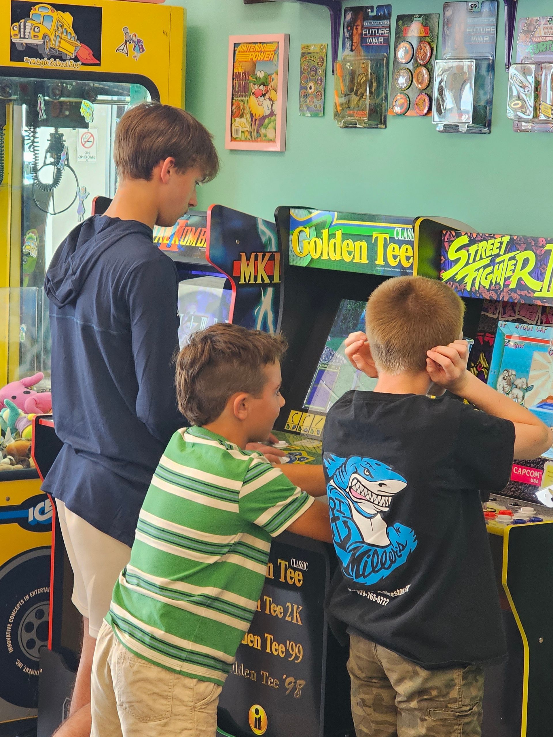 Three young boys are playing a video game in an arcade.