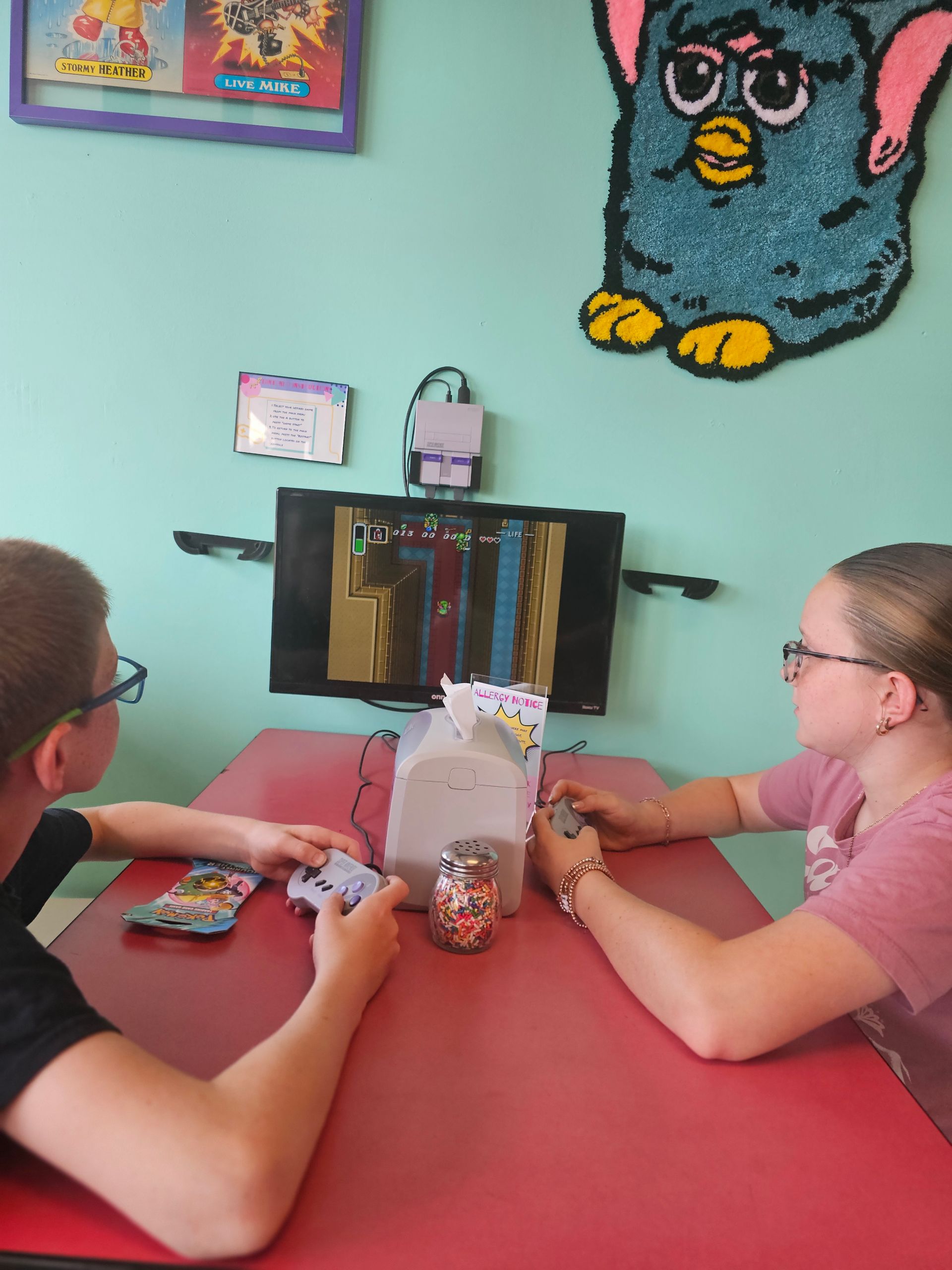 A boy and a girl are playing a game with a furby on the wall behind them