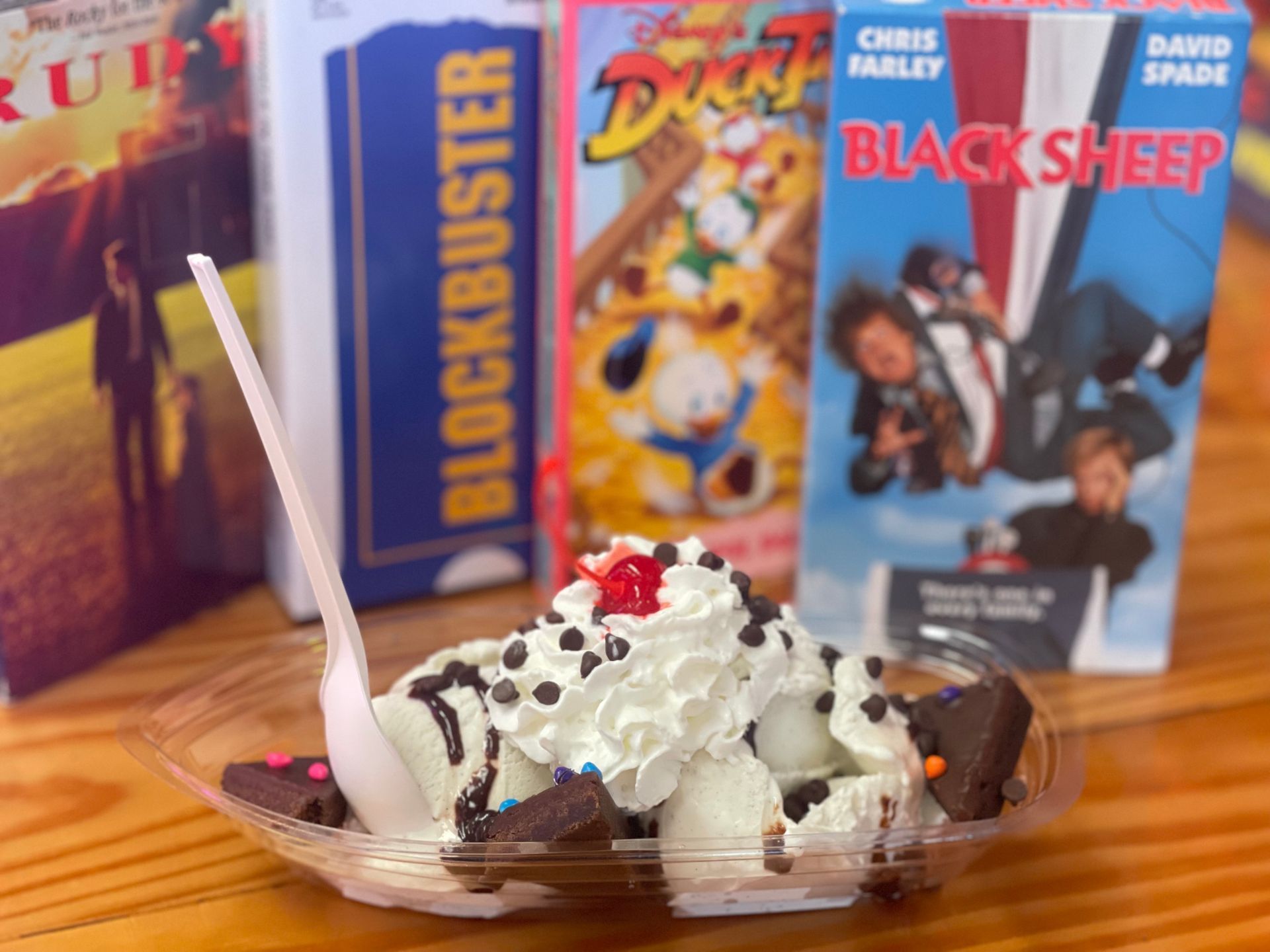A bowl of ice cream with a spoon in front of a box of blockbuster cereal