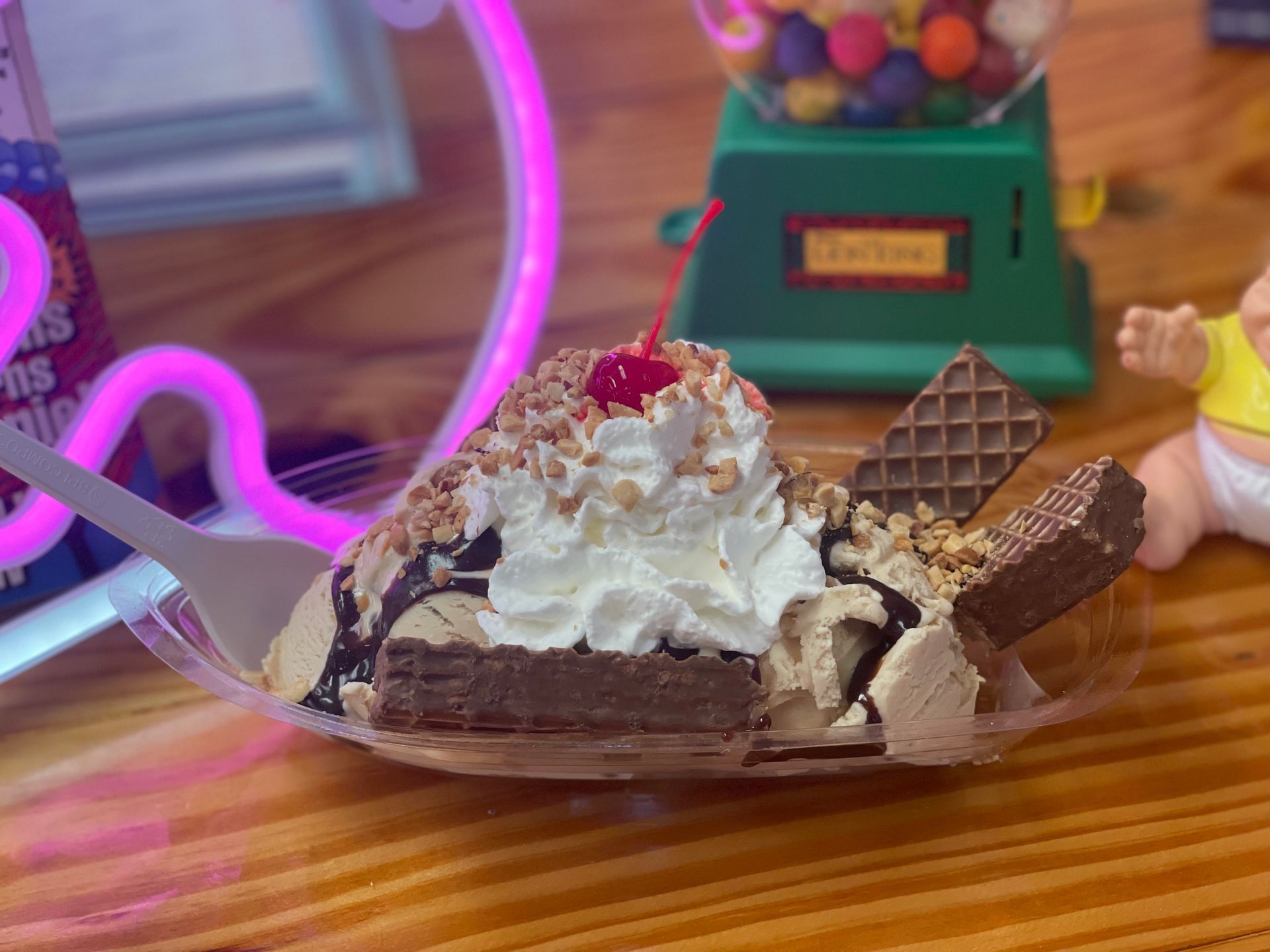 A banana split with whipped cream and a cherry on top is on a wooden table.
