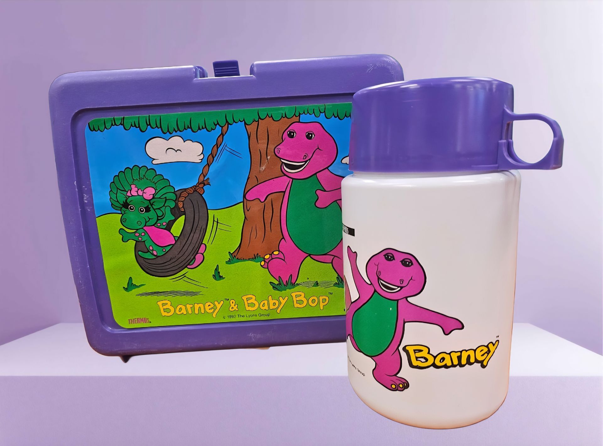 A purple lunch box and a white bottle with barney on it