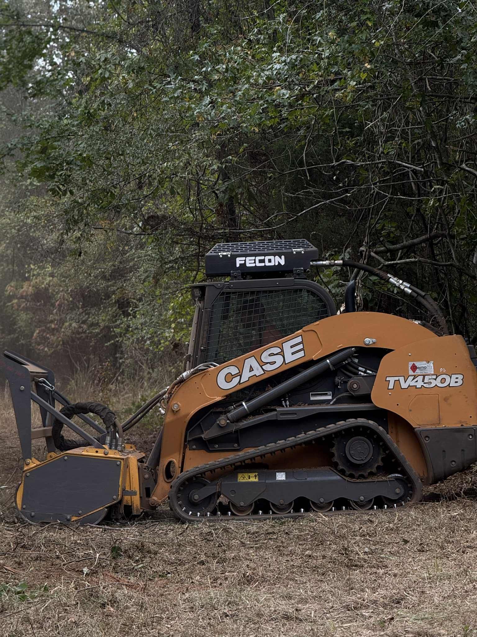 Orange CASE TV450B skid steer operating in a wooded area, equipped with a forestry mower.
