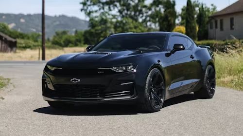 A black chevrolet camaro is parked on the side of a road.