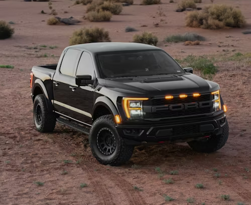 Gold classic car parked in front of a building with a white pickup truck.