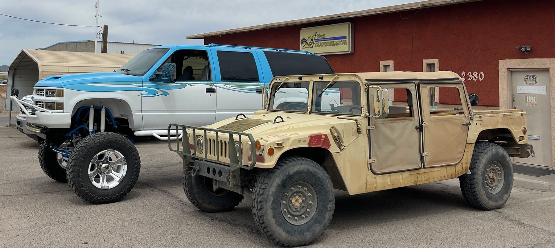 Two military vehicles are parked next to each other in front of a red building.