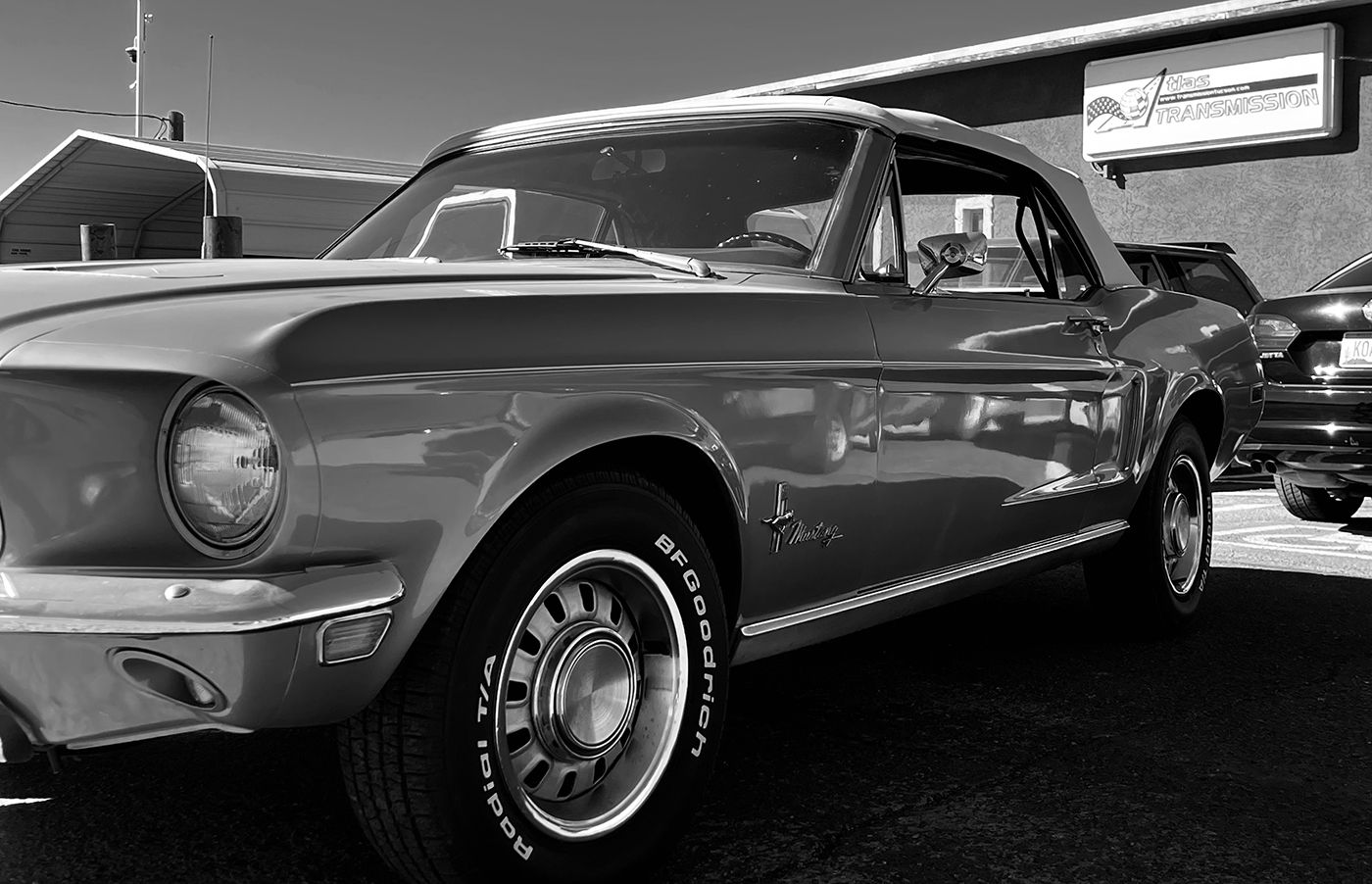 Classic Mustang convertible parked in front of a building. Black and white.