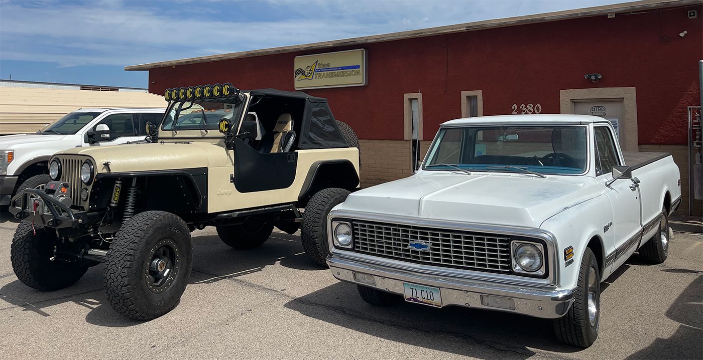 A jeep and a white truck are parked in front of a red building.