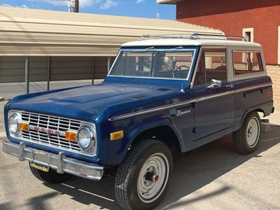 A blue and white ford bronco is parked in front of a building.