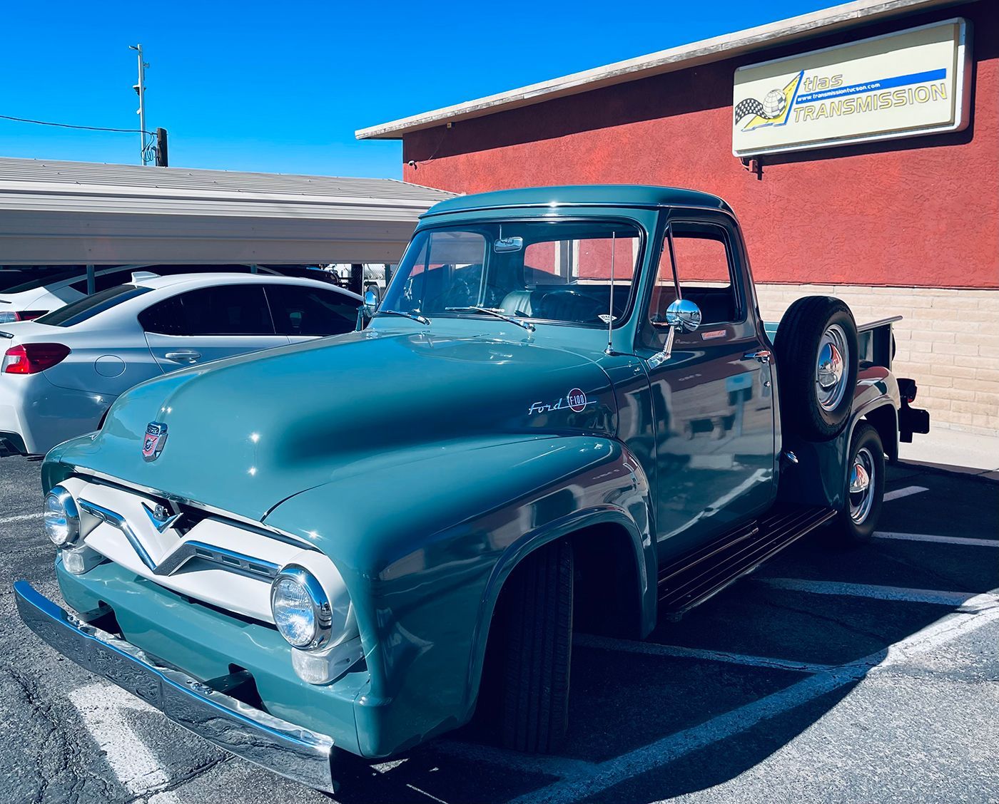 Blue vintage Ford pickup truck parked outside a building on a sunny day.