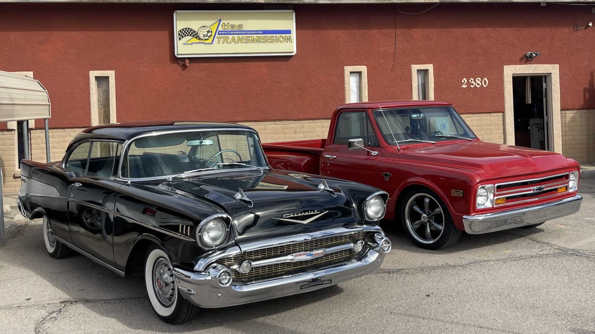 A black car and a red truck are parked in front of a building.