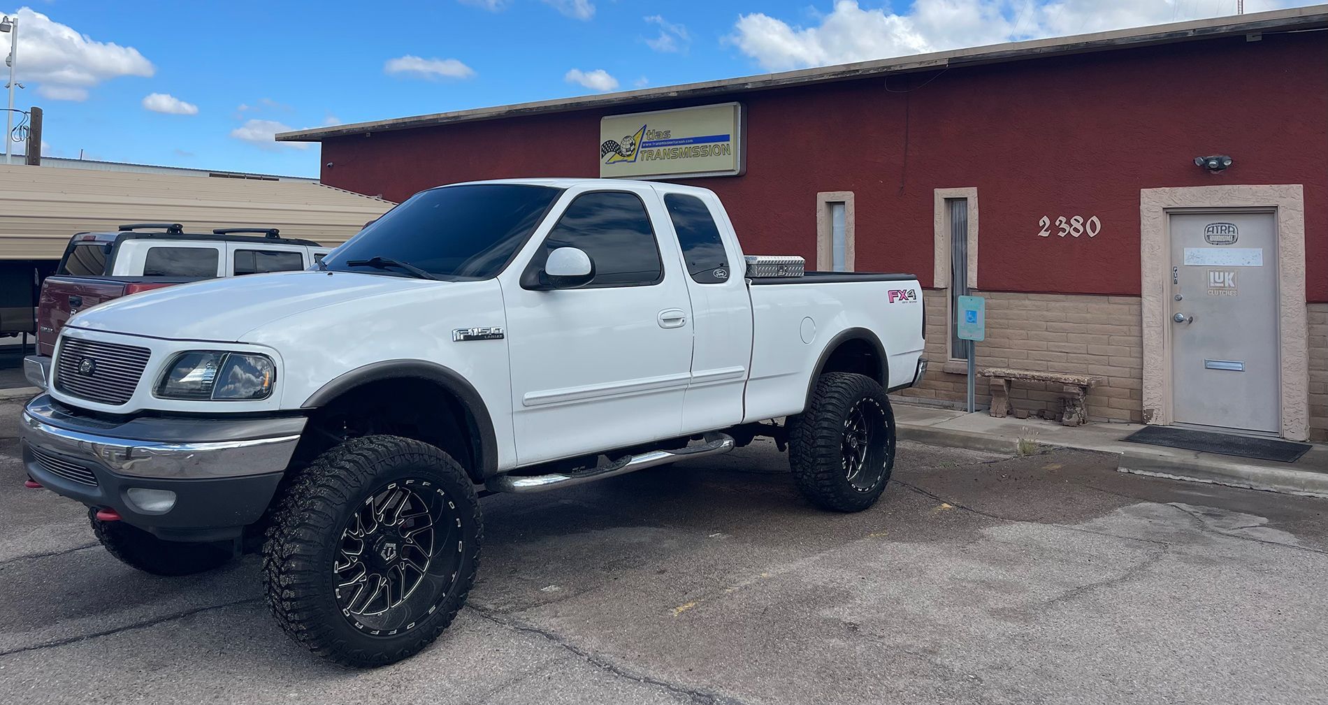 A white truck is parked in front of a red building.