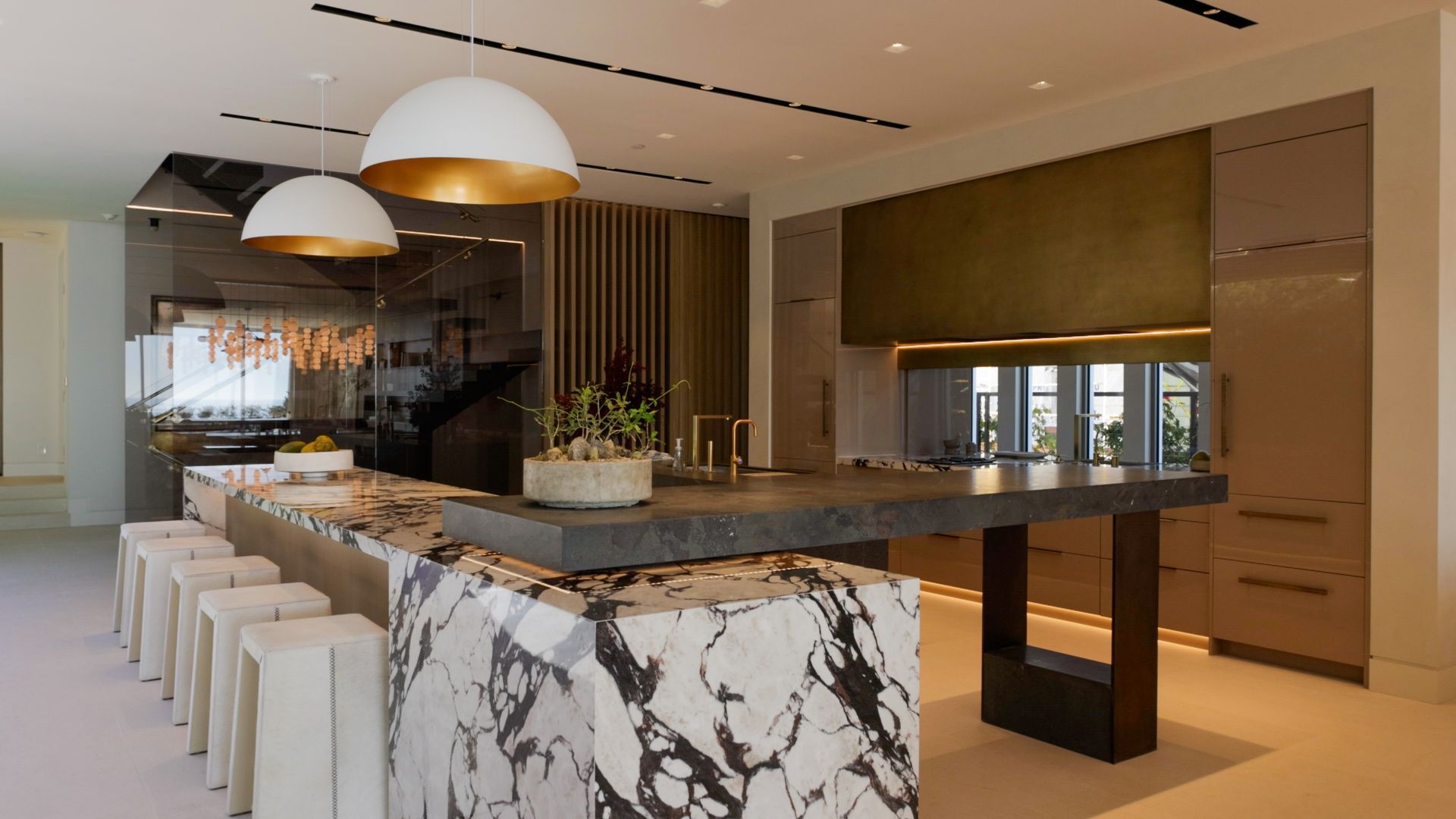 A modern kitchen with a large black-and-white marble island, seating, and gold-toned cabinetry under pendant lights.
