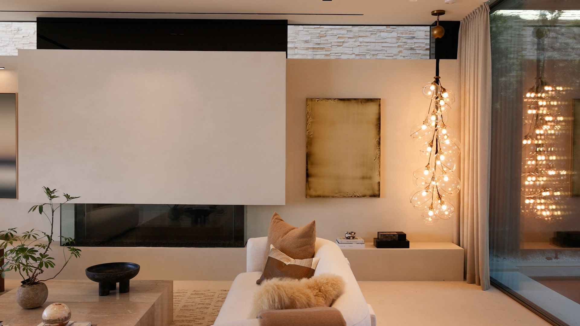 A modern living room with a white sofa, minimalist fireplace, abstract wall art, and a cascading branch-style chandelier.