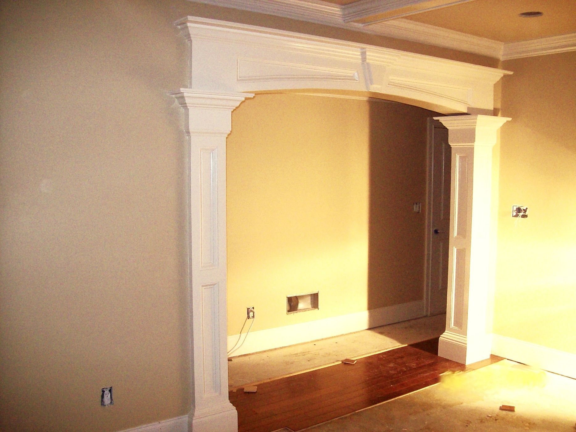 Empty room with beige walls, white columns, and a built-in alcove lit by warm sunlight.