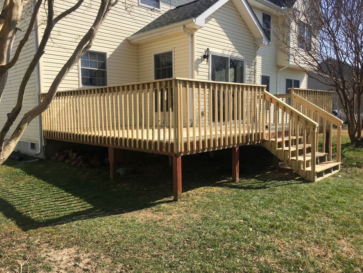 Wooden deck with stairs attached to a tan house in a grassy yard under leafless trees