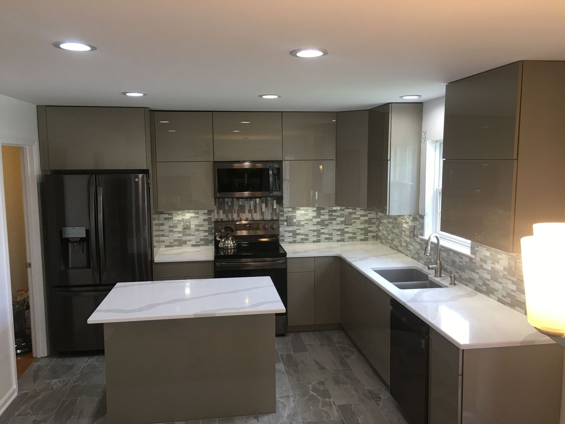 Modern kitchen with dark cabinets, white island, stainless appliances, and gray tile backsplash