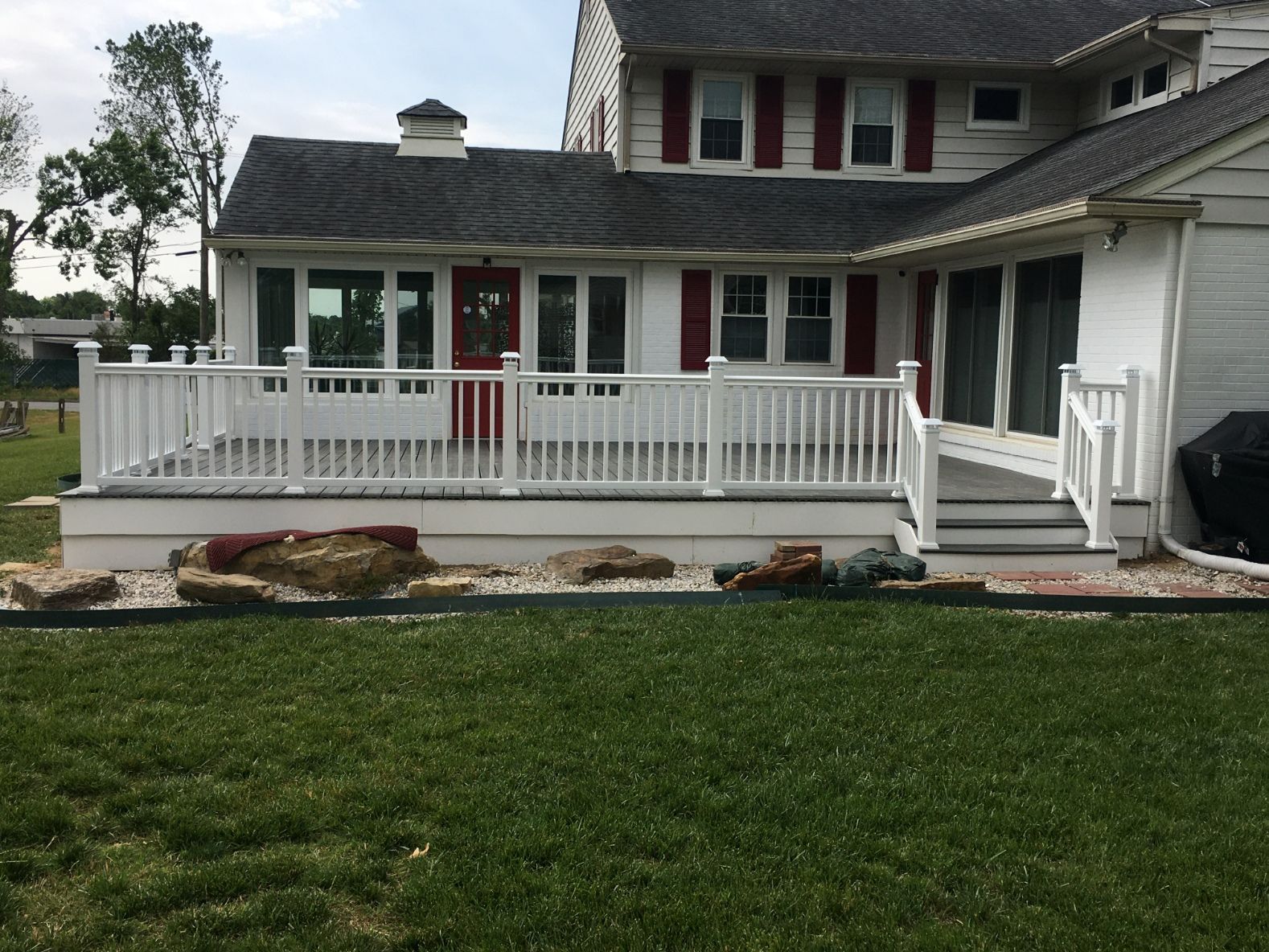 White house with a wraparound porch, red door, and green lawn in front