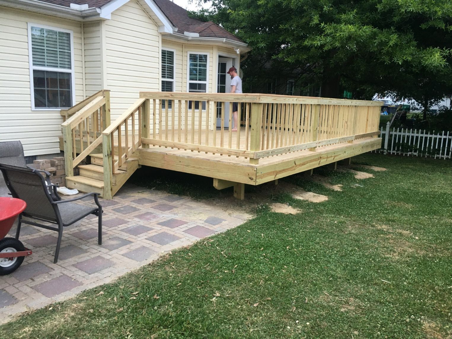 Wooden backyard deck with steps beside a house and patio chairs on a grassy lawn.