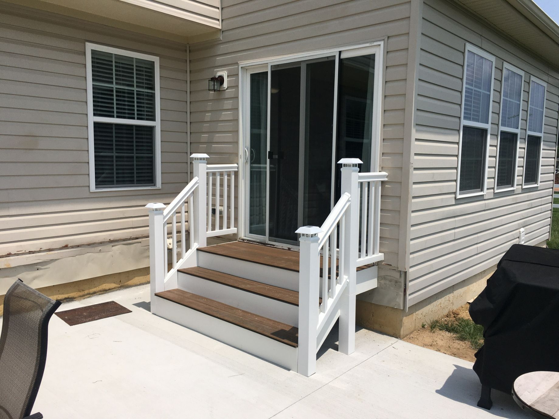 Back patio stairs with white railings leading to a sliding glass door on a beige house