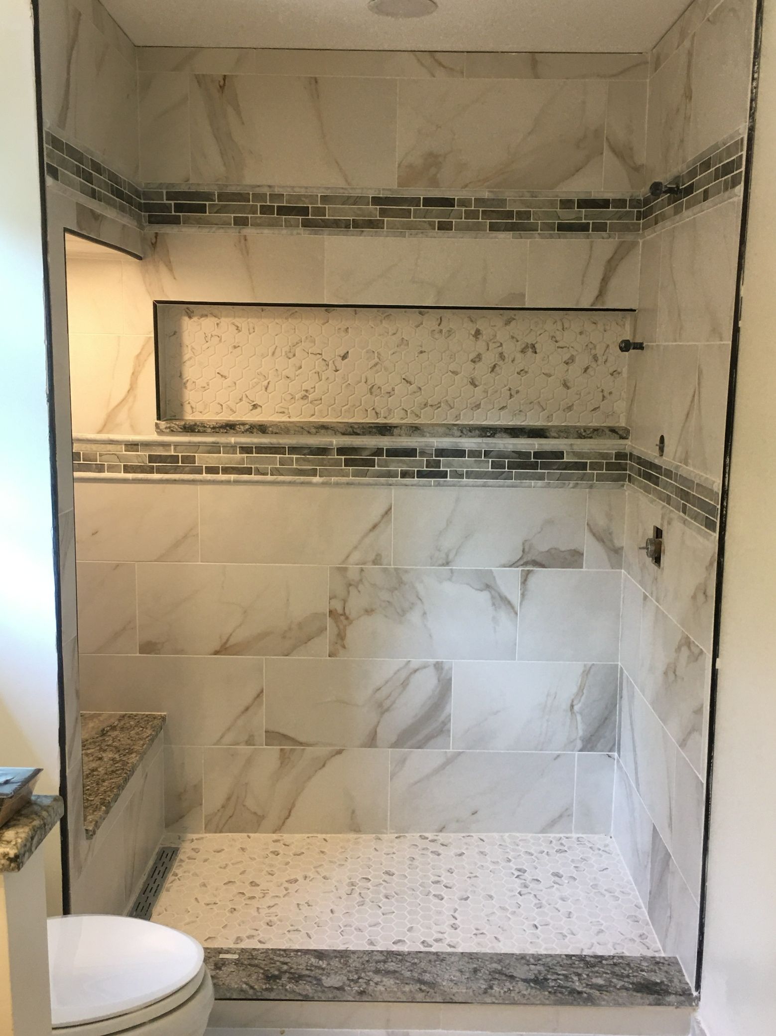 Empty tiled shower with built-in corner shelves and bench, viewed from the doorway