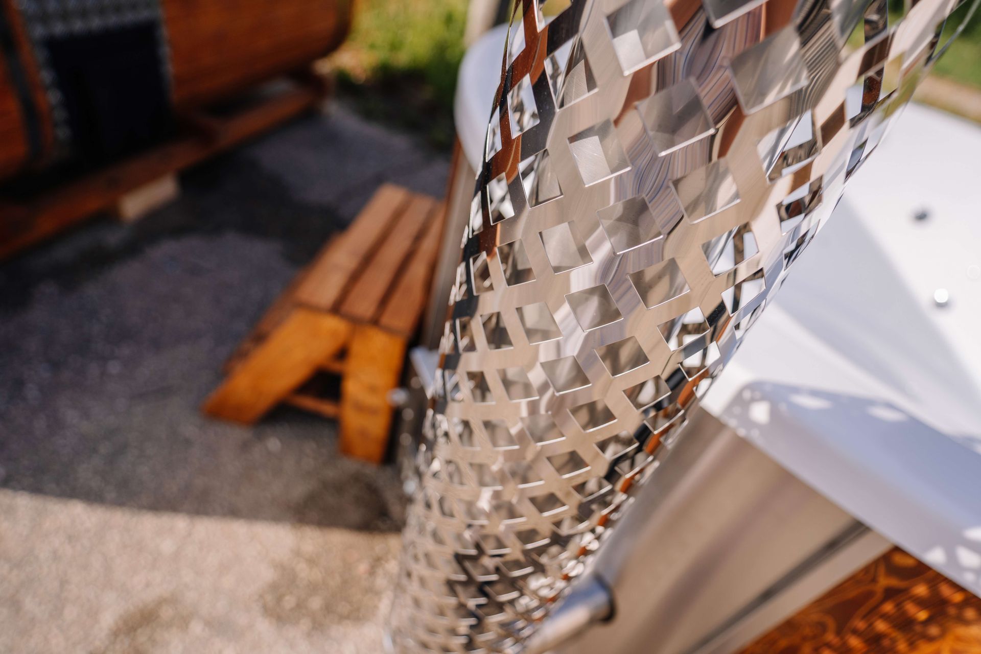 Close-up of a silver mosaic sculpture beside wooden benches and a white table outdoors